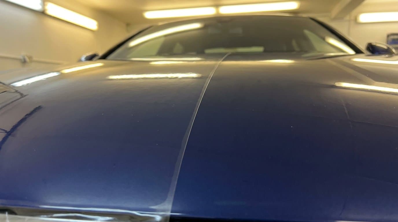 Paint protection film edge on a navy blue car bonnet in workshop