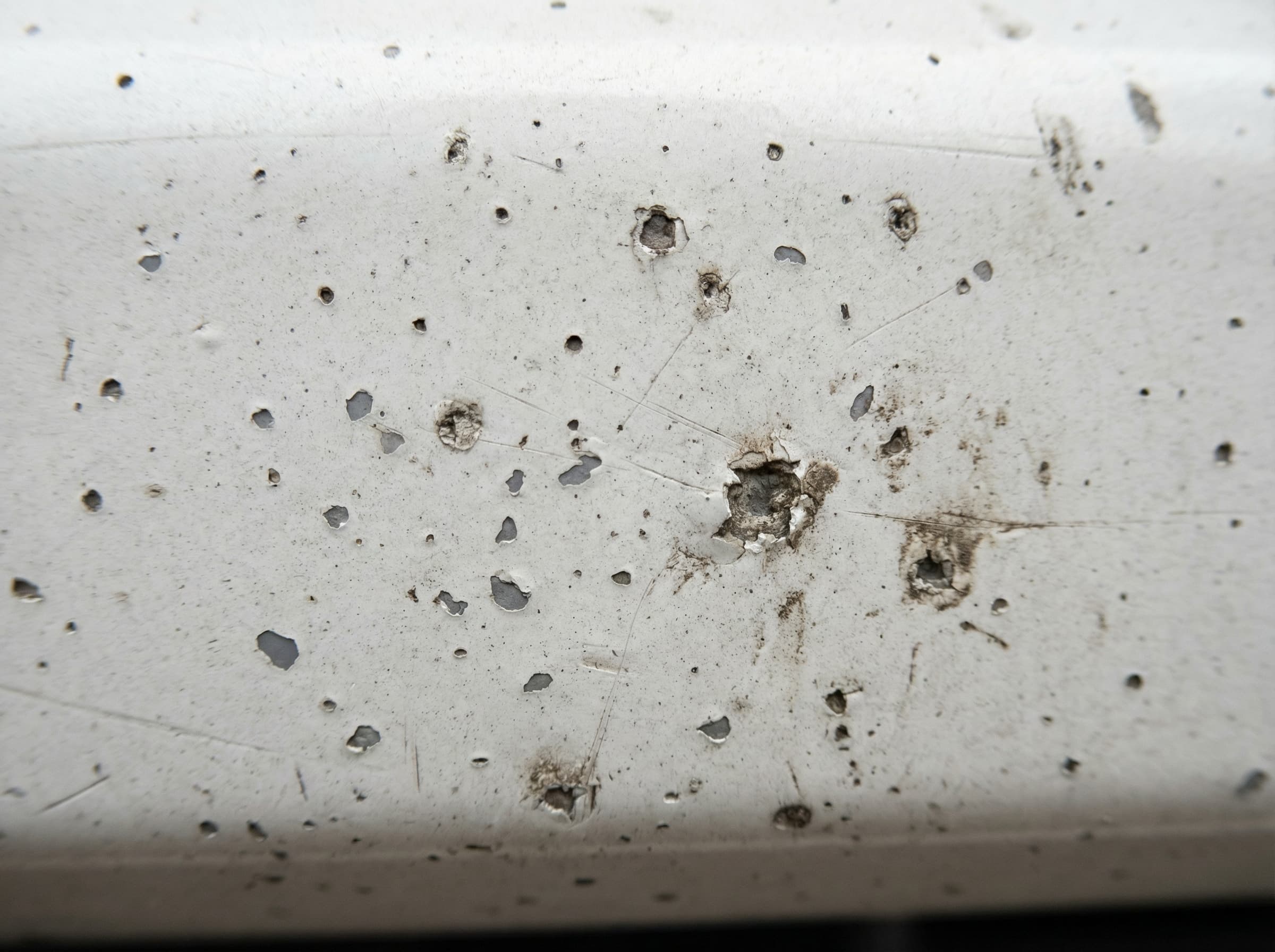 Close-up of stone chip pitting on a white car front bumper