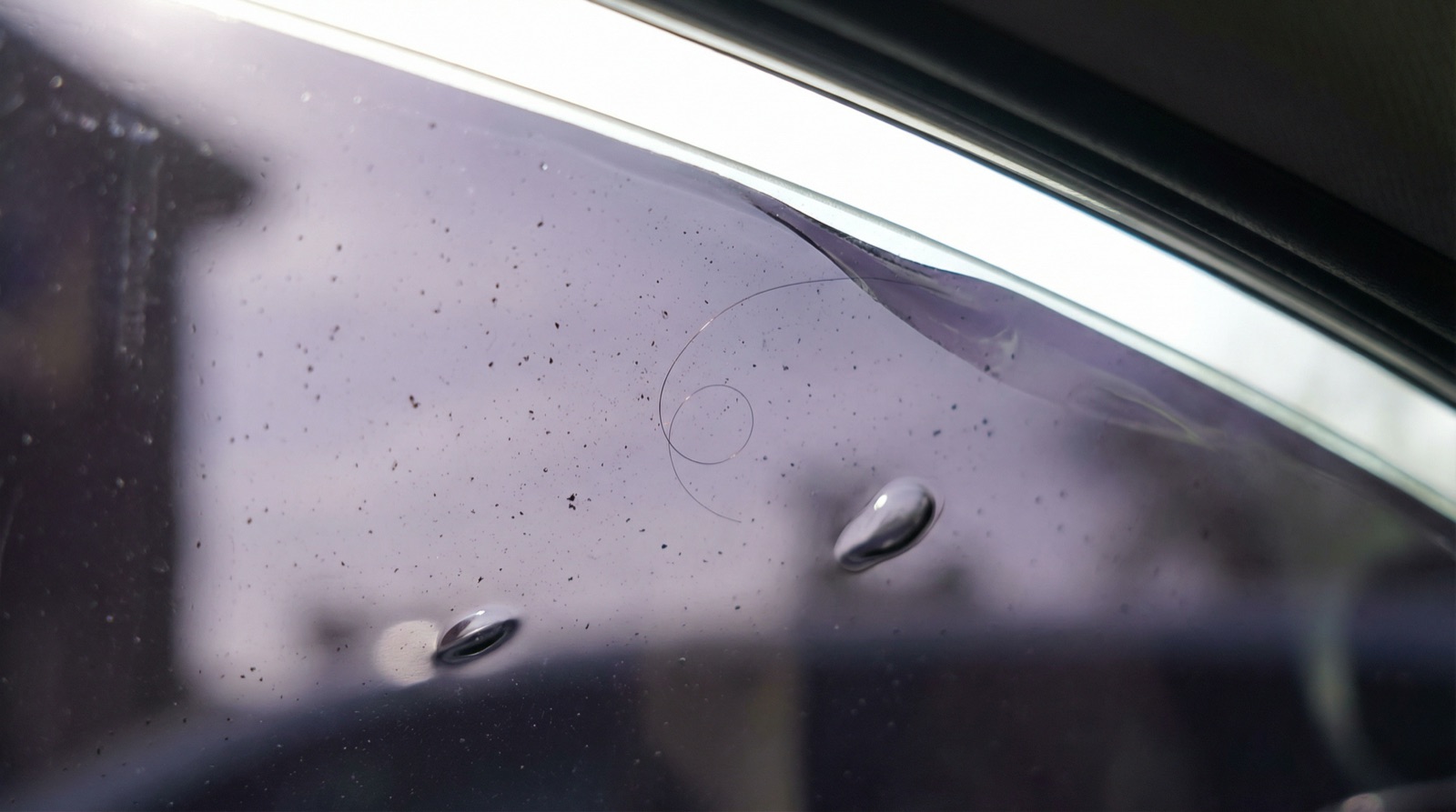 Close-up of DIY window tint showing trapped dust particles and bubbles from uncontrolled installation